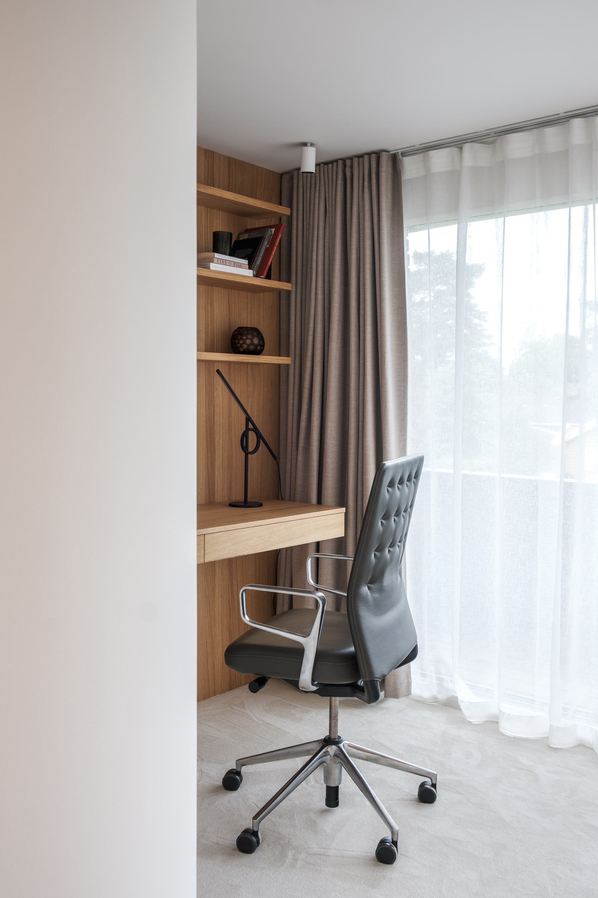 Skrivebordet i eik er bygget inn i en nisje, med hyller over og en skuffefront under platen. Åreretningen løper vannrett langs platen, og dagslyset fra vinduet legger seg mykt over overflaten.